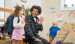 A parent kneels to hug a toddler goodbye while a smiling teacher waits nearby in a bright Willowdale classroom